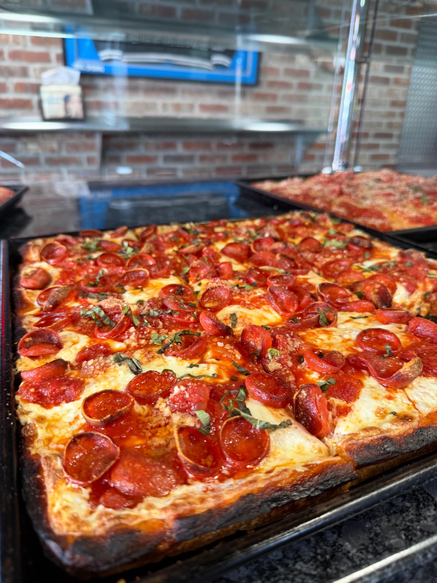 Square pepperoni Sicilian pizza topped with fresh basil